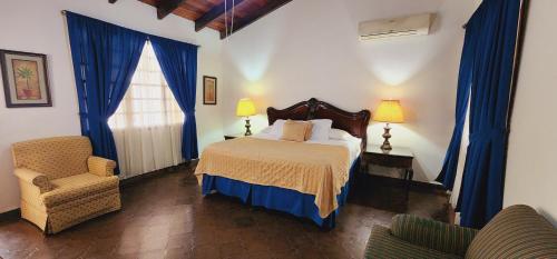 1 dormitorio con 1 cama con cortinas azules y silla en Camila´s Hotel en San Pedro Sula