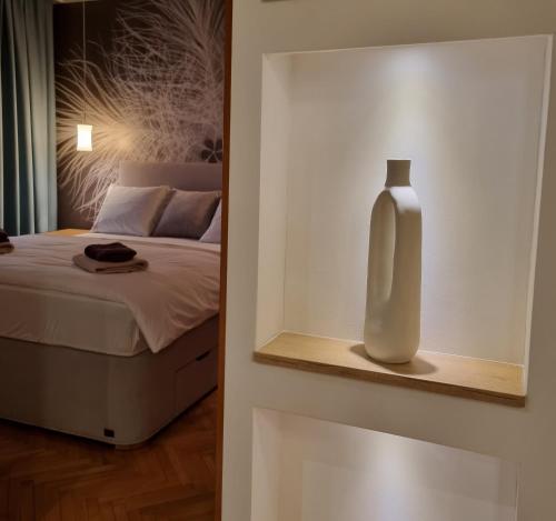 eine weiße Vase auf einem Regal neben einem Bett in der Unterkunft Apartman Centar in Kraljevo