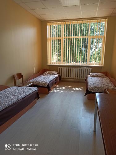Habitación con 3 camas y ventana grande. en Kriaunų bendruomenės Svečių namai, en Gipenai