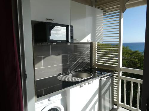 a kitchen with a sink and a television on a balcony at Appartement terrasse vue mer et piscine in Le Diamant