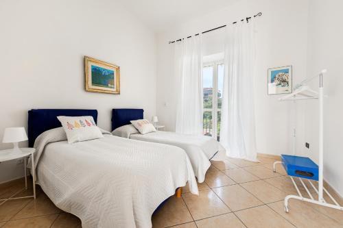 two beds in a white room with a window at La casa di Ele 2-100 metri dalla Reggia in Caserta