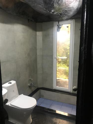 ein Bad mit einem WC und einem Fenster in der Unterkunft Rai’s Coorg Cave House in Madikeri
