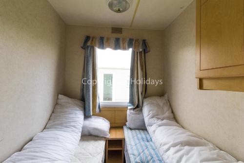 two beds in a small room with a window at 8 Berth Caravan At California Cliffs Holiday Park In Norfolk Ref 50007d in Great Yarmouth