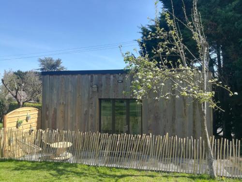 a wooden house with a fence and a tree at Le Gîte insolite Gonnedouillé in Gonneville-en-Auge