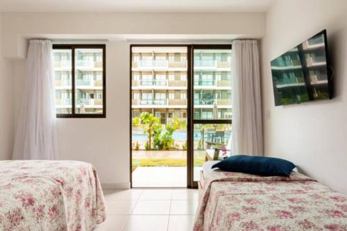 a bedroom with two beds and a large window at Mana Beach Muro Alto-Flat 12 Ohana e 20 Aloha Térreo Frente Piscina in Porto De Galinhas