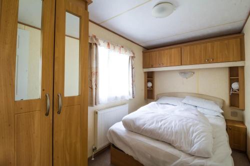 a bedroom with a bed and wooden cabinets and a window at 8 Berth Caravan For Hire At California Cliffs Holiday Park In Norfolk Ref 50046l in Great Yarmouth