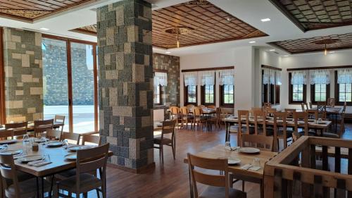 un restaurante con mesas y sillas de madera y ventanas grandes en Pupa Winery Serene Stay, en Berat