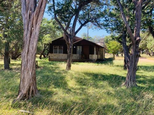 a house in the middle of a field with trees at The Camp Blanco by Lodgewell - Riverfront retreat 2 Homes, Bunk House, Game Room & more in Blanco