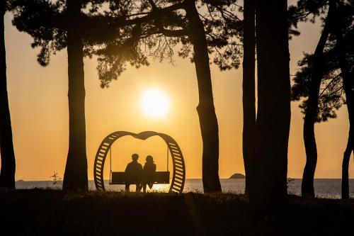 a couple sitting on a bench in front of the sunset at C-One Resort Jaeundo in Sinan