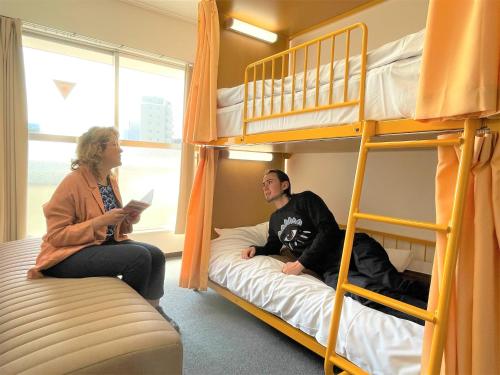 a man and a woman sitting in a room with bunk beds at Sakura Hotel Nippori in Tokyo