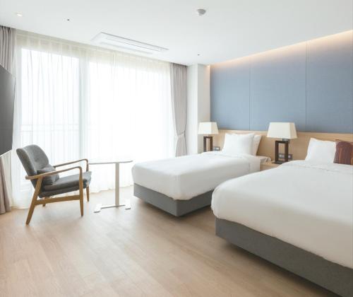a hotel room with two beds and a chair at C-One Resort Jaeundo in Sinan