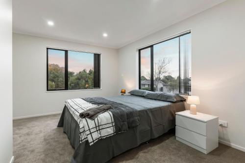 a bedroom with a large bed and two windows at Jupiter St Holiday Home No 3 in Auckland