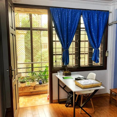 a desk in front of a window with a blue curtain at Rainbow HomeStay - No 8 Alley 18B Tong Dan in Hanoi