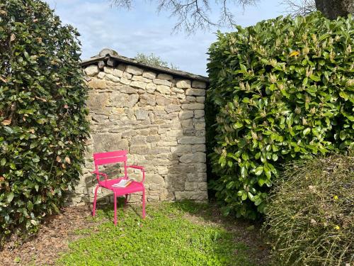 une chaise rouge assise devant un mur en pierre dans l'établissement Vacances aux Petites Rivières, à Saint-Loup-de-Saintonge