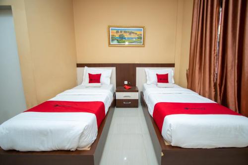 two beds in a hotel room with red pillows at RedDoorz Syariah @ Jalan Gajah Mada Meulaboh in Meulaboh