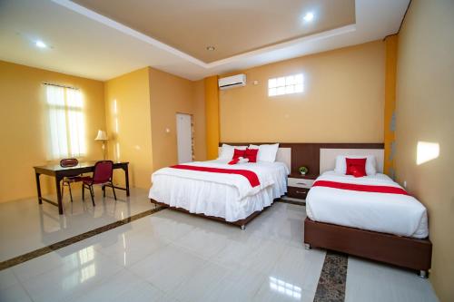 a bedroom with two beds and a table and a desk at RedDoorz Syariah @ Jalan Gajah Mada Meulaboh in Meulaboh