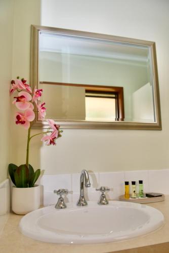 a bathroom sink with a mirror and a vase with flowers at Green Gables Warburton - King Garden Suite in Warburton