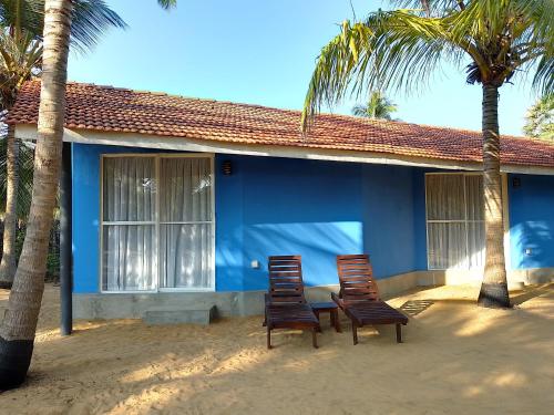 two chairs sitting outside of a blue house with palm trees at Nayan's Paradise in Kottanitivu