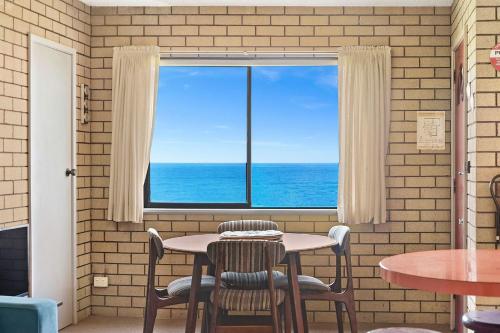 a table and chairs in front of a window with the ocean at 1 15 Dalmeny Drive Kianga in Kianga