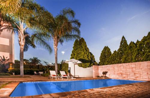 a swimming pool with two chairs and palm trees at Golden Horse Hotel in Pietermaritzburg