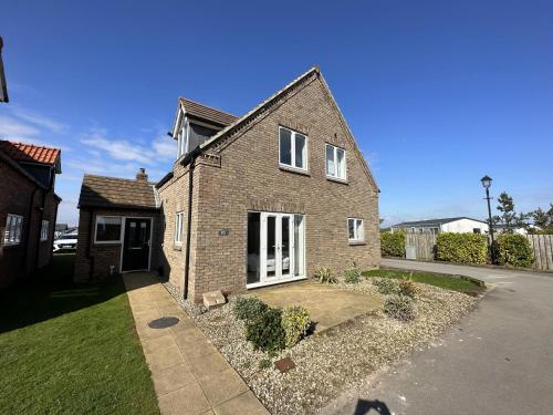 a brick house with white doors on a street at Echo Beach - Sleeps 12 - Part of the The Bay Filey Holiday Village with pool, gym and direct beach access, pub, restaurant, tennis and meadows walks in Filey