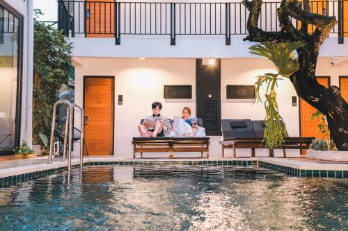 a man and woman sitting on a bench next to a swimming pool at Sathu Hotel in Chiang Mai