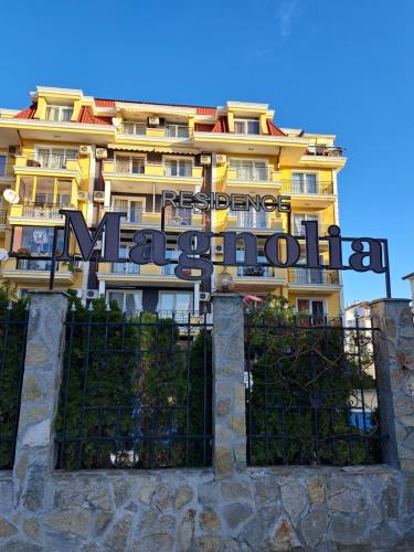 a yellow building with a sign in front of it at Апартамент за гости Магнолия Резиденс in Sunny Beach