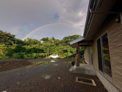 a rainbow in the sky over a house with a car at Yakunoyado Taguchi in Yakushima