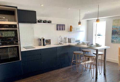 a kitchen with blue cabinets and bar stools at Beach House Apartment 1 - St. Ives harbour front apartment with stunning views in St Ives