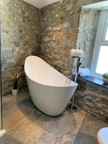 a bath tub in a bathroom with a stone wall at Beach House Apartment 1 - St. Ives harbour front apartment with stunning views in St Ives