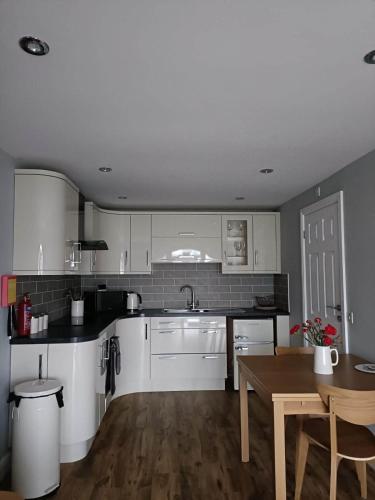 a kitchen with white cabinets and a wooden table at Bwthyn Eira in Llangefni