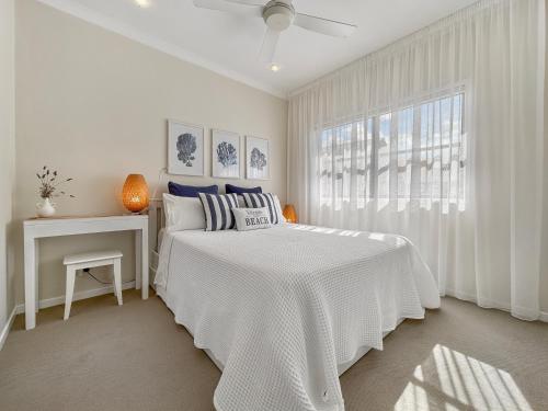a white bedroom with a white bed and a window at Serene Beachside Apartment in Marcoola