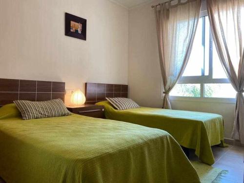 een slaapkamer met 2 bedden met groene lakens en een raam bij Acogedor apartamento cerca de la playa in Los Alcázares