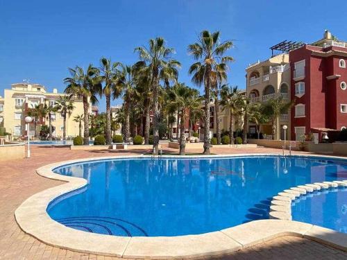 uma grande piscina azul com palmeiras e edifícios em Acogedor apartamento cerca de la playa em Los Alcázares