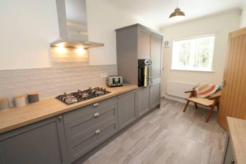 uma cozinha com armários cinzentos e um forno com placa de fogão em The Cottage IH3ATL em Stockton-on-Tees