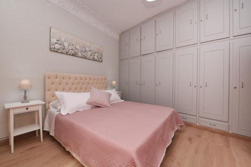 una camera da letto con un letto con copriletto rosa e armadi bianchi di Nefeli House Syros a Ermoupoli