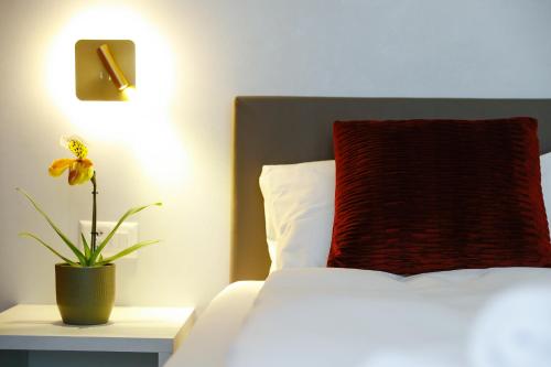 a bed with a red pillow and a plant on a table at Boutique Hotel Piazza Grande in Locarno