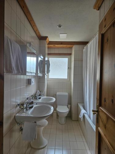 a bathroom with two sinks and a toilet and a window at Hotel Schweizerhof Pontresina in Pontresina