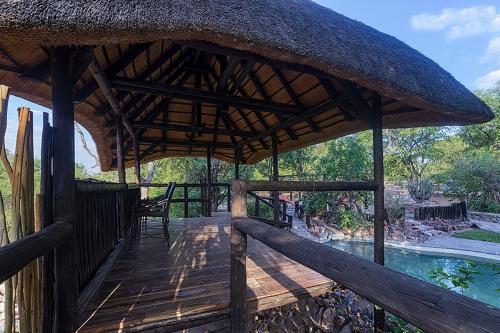 a wooden deck with a thatched roof and a swimming pool at Hobatere lodge in Otjovasandu