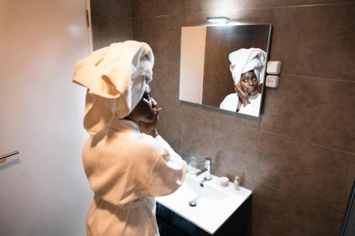 Una mujer con una toalla en la cabeza mirando en el espejo del baño. en Hotel Nina, en Dakar