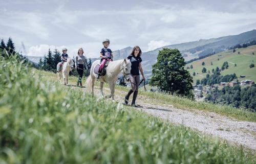 three children riding on horses on a dirt road at Familienresort Ellmauhof - das echte All Inclusive in Saalbach Hinterglemm
