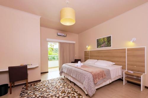 a bedroom with a bed and a desk and a window at Hotel Fazenda Dona Francisca in Joinville