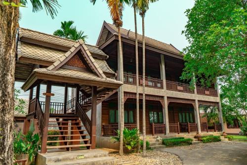 a house with a wrap around porch and palm trees at มนต์เมืองเชียงใหม่ รีสอร์ต Monmuang Chiangmai Resort in Hang Dong