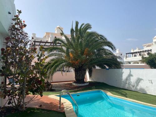 a swimming pool with a palm tree next to a building at Royal Park Guesthouse in Corralejo