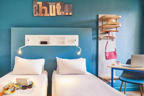 two beds in a room with a desk and a laptop at ibis budget Saint-Ouen-l'Aumône in Saint-Ouen-lʼAumône