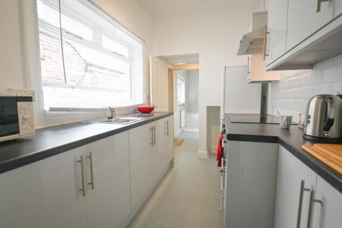 a kitchen with white cabinets and a sink and a window at Clarice House by YourStays, 3 bedroom house by University of Staffordshire in Stoke on Trent