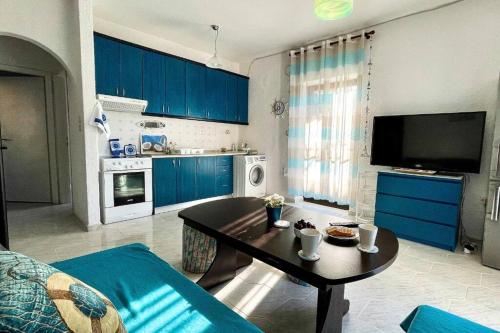 a living room with a table and a kitchen with blue cabinets at Apartment with sea view in Pefkohori. in Pefkohori
