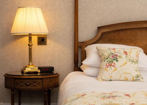 a bedroom with a bed with a lamp on a table at Cally Palace Hotel & Golf Course in Gatehouse of Fleet