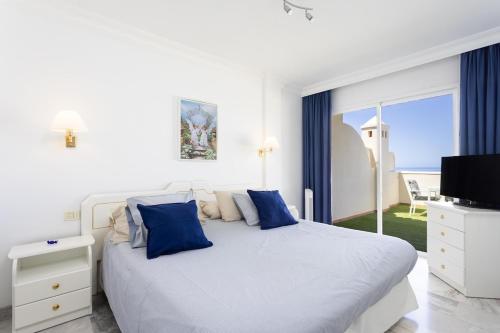 - une chambre blanche avec un grand lit et des oreillers bleus dans l'établissement EDEN RENTALS Fabulosas Vistas al Mar y Los Acantilados, à Acantilado de los Gigantes