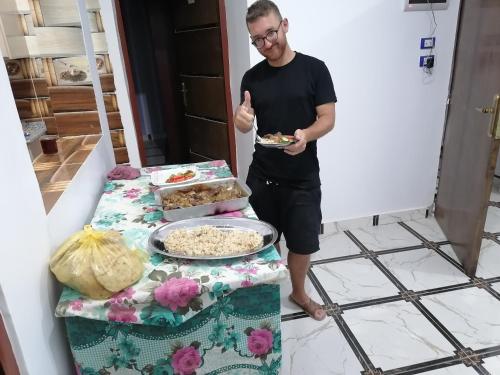 un homme tenant une assiette de nourriture à côté d'une table dans l'établissement Zohra Guest House, à Assouan